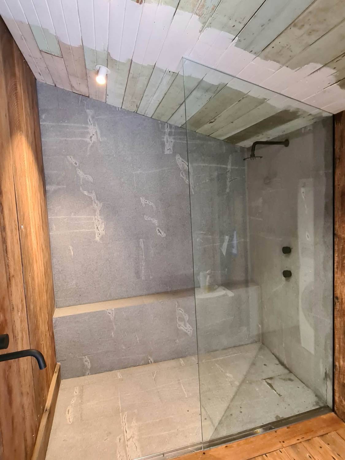 Frameless fixed glass panel in a stone walk-in shower