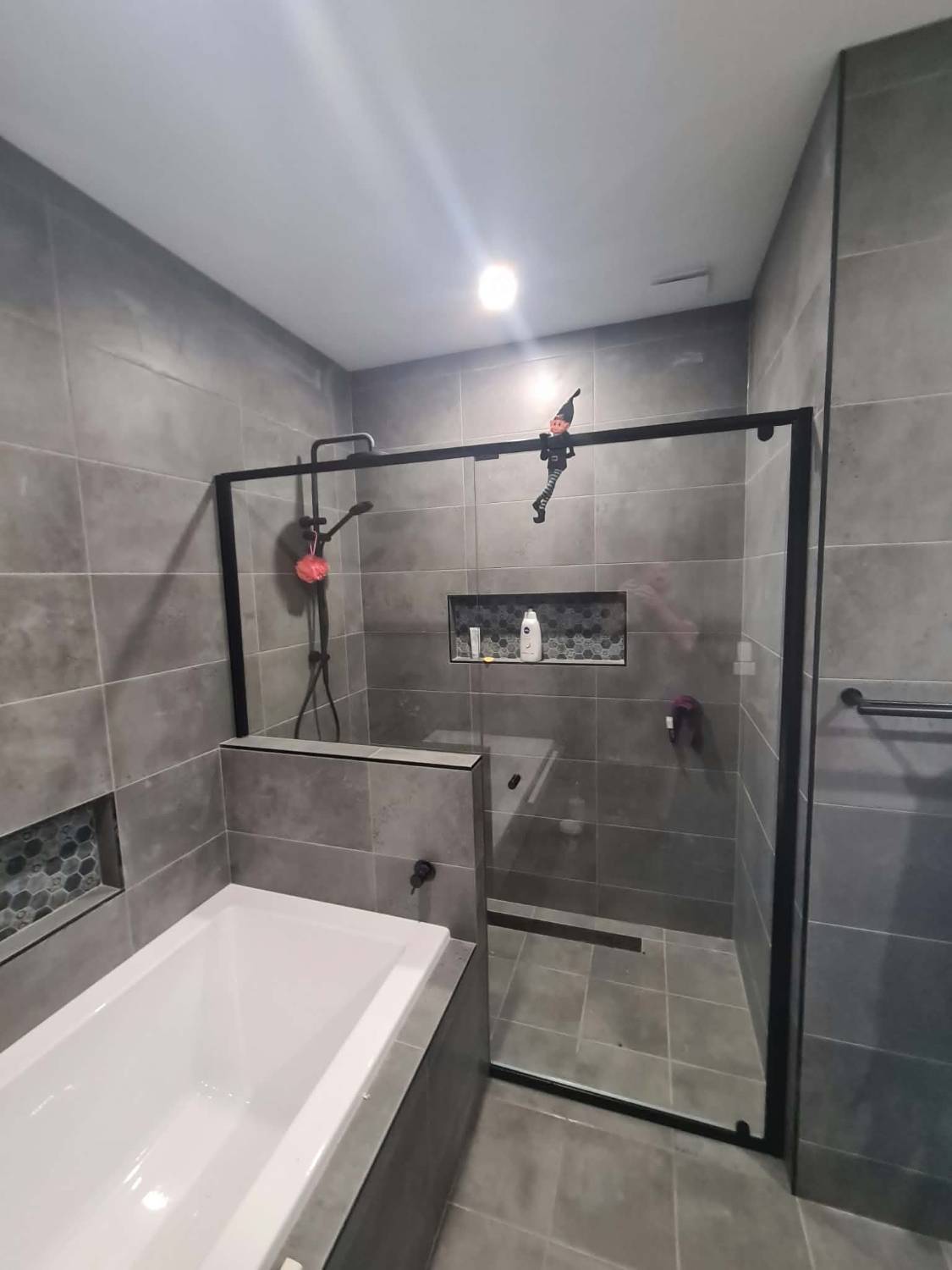Semi-frameless shower screen with a matte black frame built over a tiled hob beside a bath